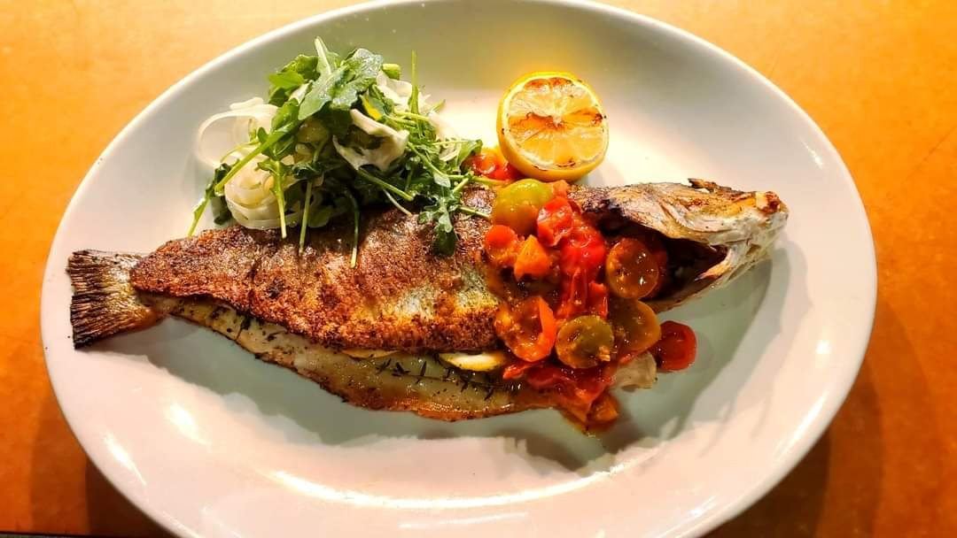 Whole roasted branzino plated with arugula and blistered tomatoes