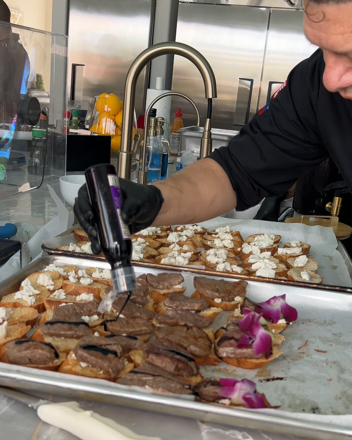 Chef Oscar finishing trays of herb-grilled beef crostini with balsamic reduction and orchids
