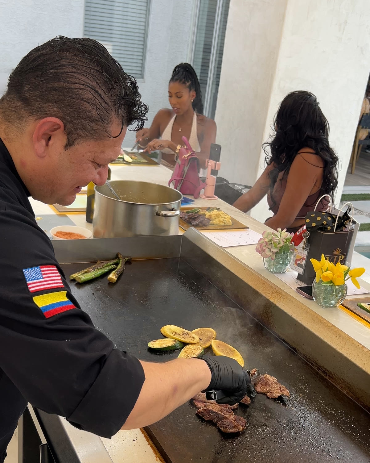 Chef Oscar Sanchez grilling ribeye and vegetables on an outdoor hibachi griddle at Sip & Dip, guests seated along the bar behind him